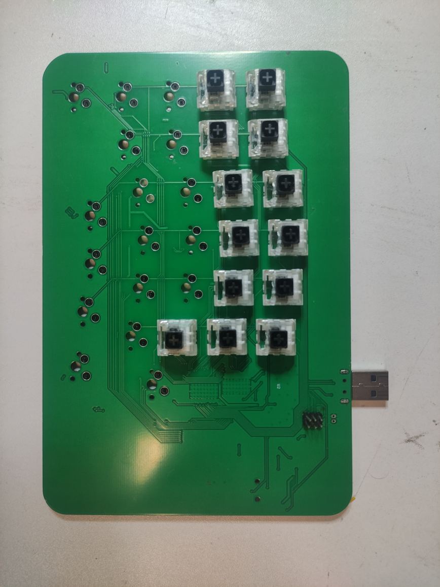 The built keyboard half on green solder mask, partially populated with mechanical switches in hot-swap sockets, with a USB plug soldered to the board edge